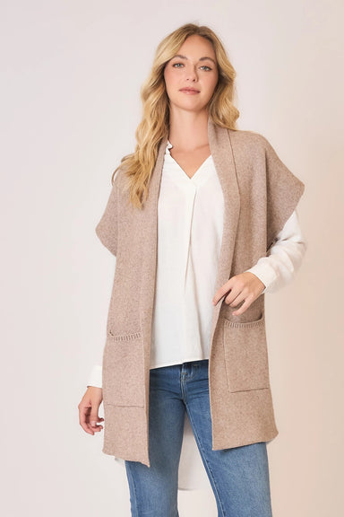 Woman wearing a beige cardigan over a white shirt and blue jeans on a plain background