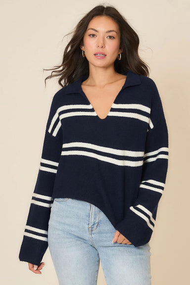 Woman wearing a navy sweater with white stripes and light blue jeans on a beige background