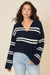 Woman wearing a navy sweater with white stripes and light blue jeans on a beige background