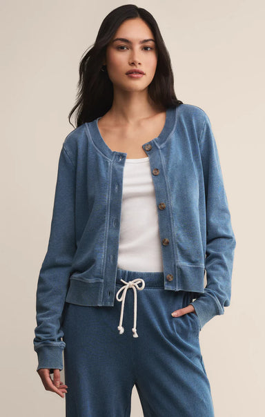 Woman wearing a blue denim cardigan over a white top with matching pants on a beige background