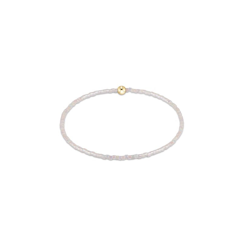 Thin white beaded bracelet with a gold clasp on a white background