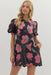 Woman wearing a black dress with pink floral patterns on a white background