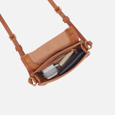 Brown leather crossbody bag with visible contents on a white background