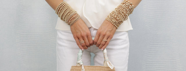 Person wearing gold e newton classic bracelets and holding a small bag against a plain background