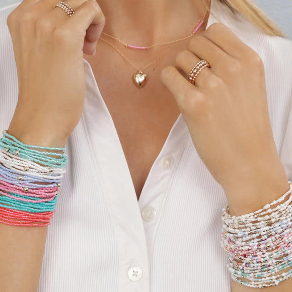 Person wearing colorful e newton bracelets and a necklace with a light blue background and 'hope unwritten' text.