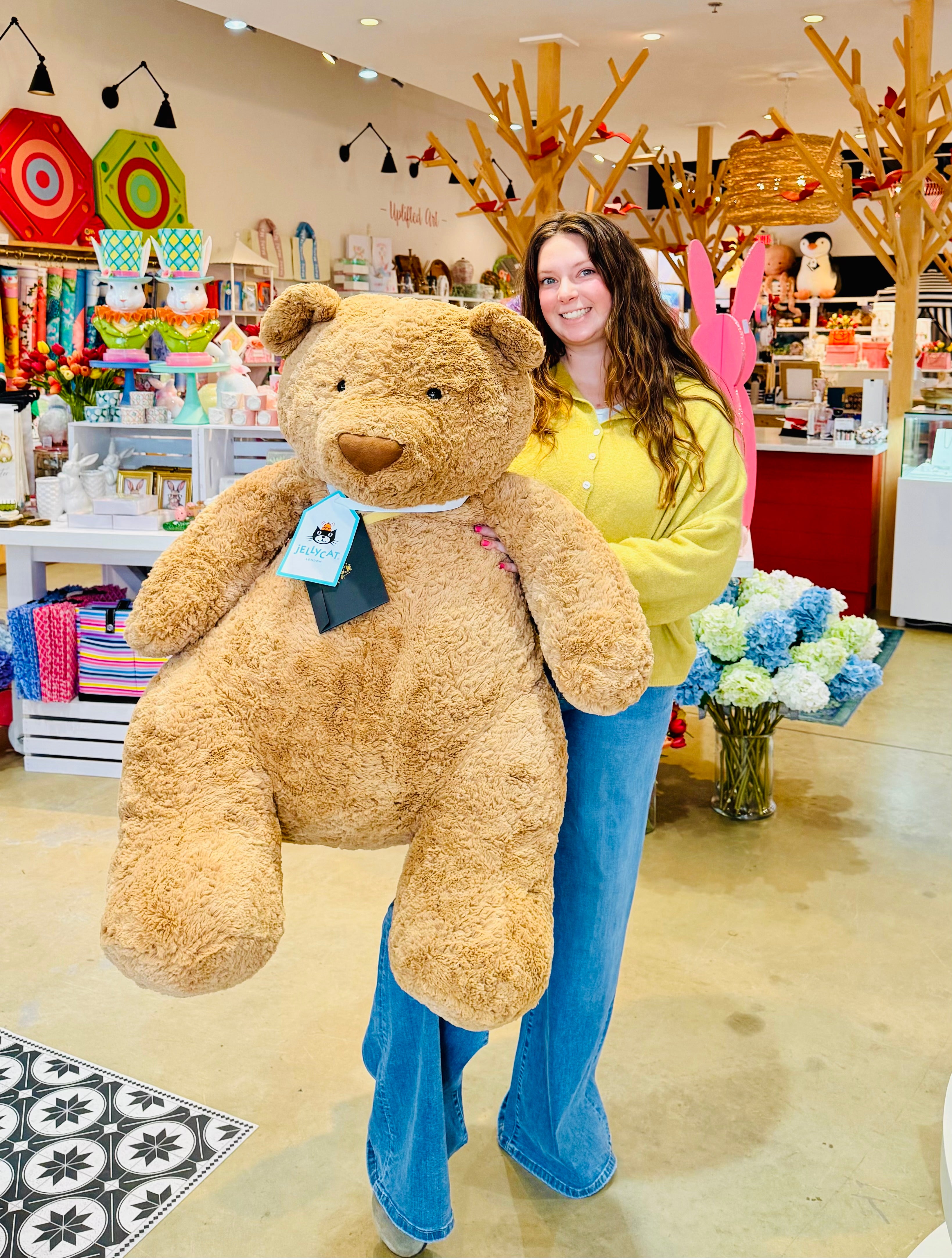 Woman holding a large teddy bear in a store with colorful decorations.