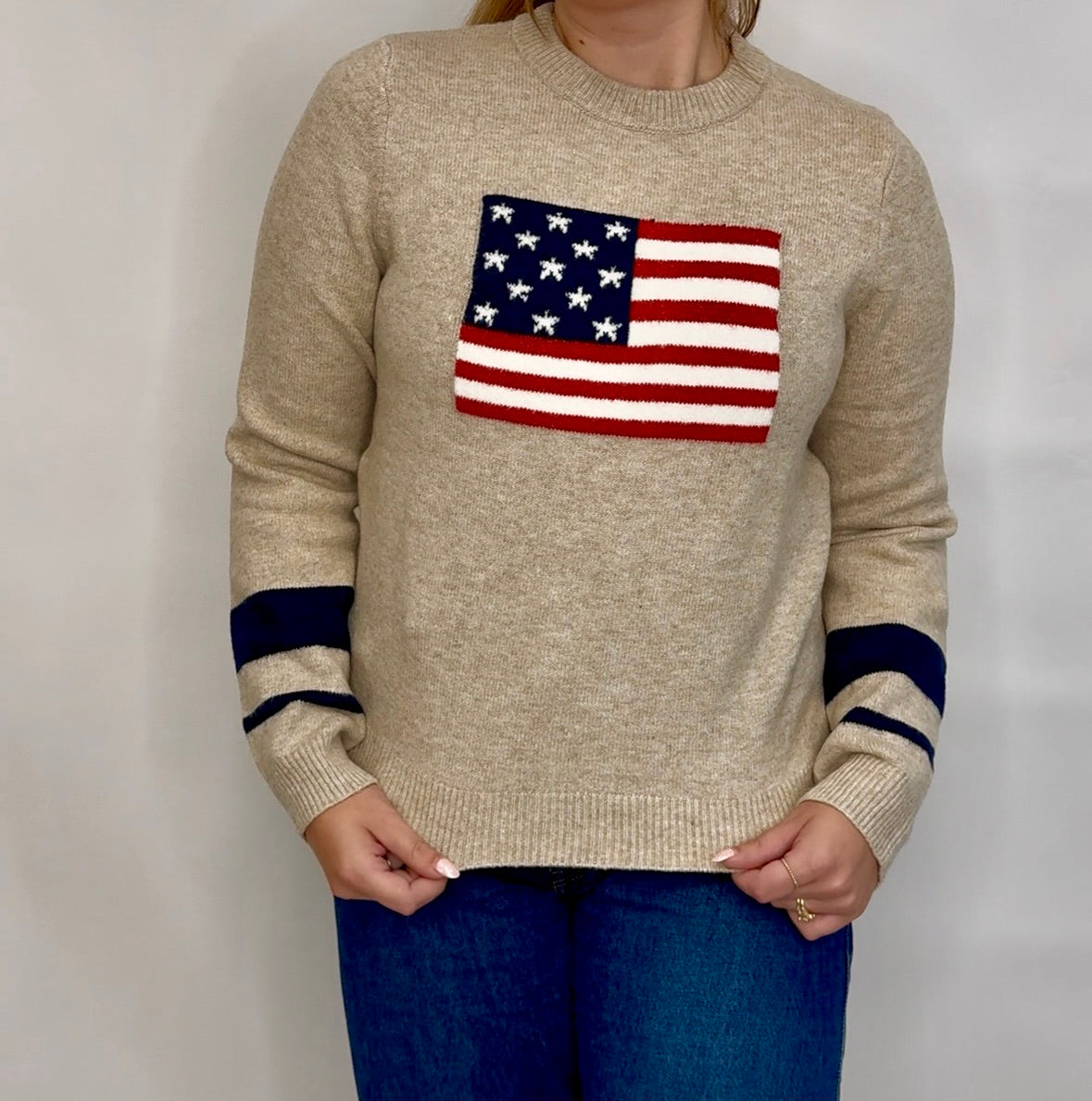 Beige sweater with American flag design worn by a person against a plain background