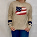 Beige sweater with American flag design worn by a person against a plain background
