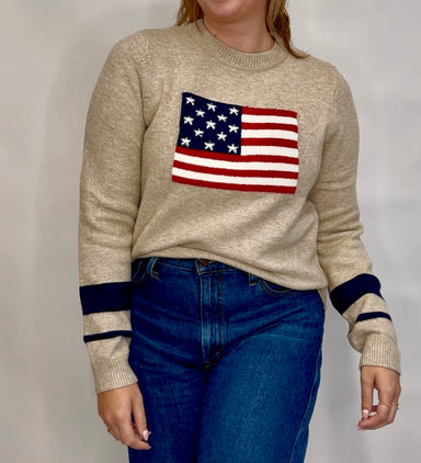 Person wearing a beige sweater with an American flag design on a plain background