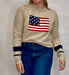 Person wearing a beige sweater with an American flag design on a plain background