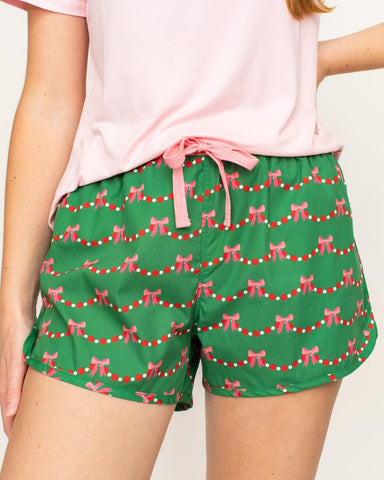 Green shorts with pink bow pattern worn by a person against a neutral background