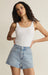 Woman wearing a white tank top and light blue denim shorts on a beige background