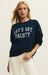 Woman wearing a navy sweatshirt with 'LET'S GET YACHTY' text on a beige background