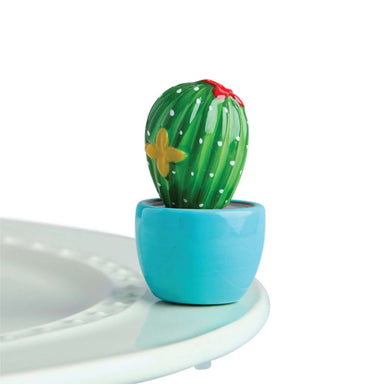 A hand-painted ceramic cactus mini figurine in green, red, and white colors, designed to sit in a dishwasher-safe base piece.