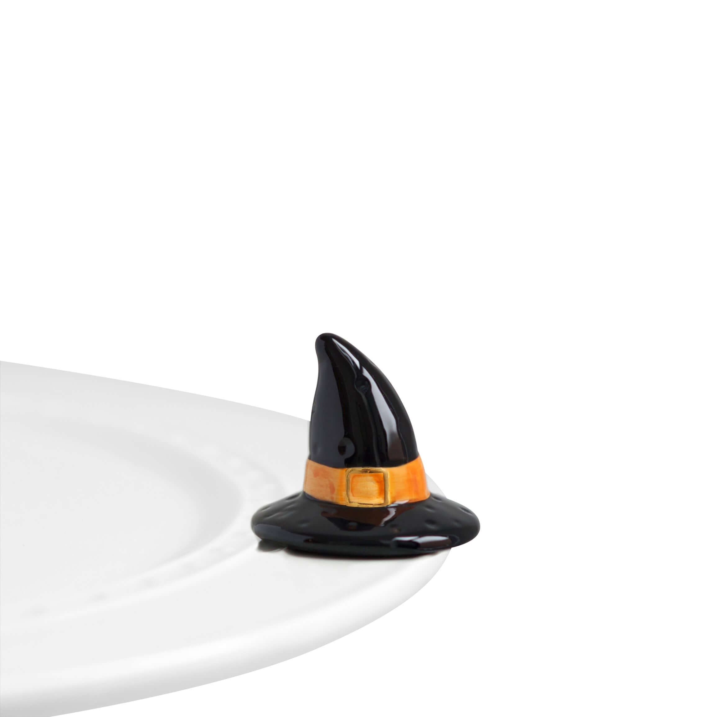 A ceramic Nora Fleming Witchful Thinking Mini figurine, resembling a black witch's hat with an orange band, placed on a white surface.
